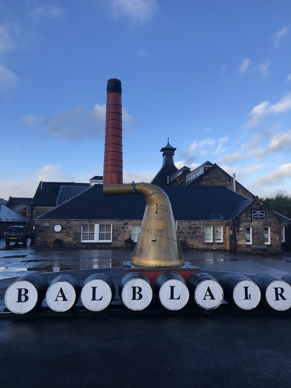 Cask ends spelling out Balblair at the Highland distillery, with a copper still and chimney behind